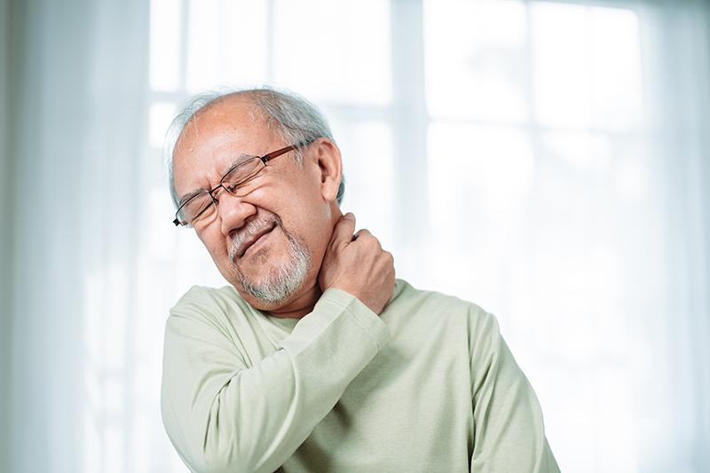 Elderly man holding his neck while experiencing neck pain.