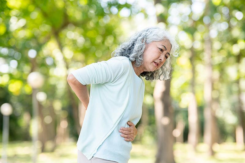 Elderly woman experiencing lower back pain while walking due to spinal stenosis.