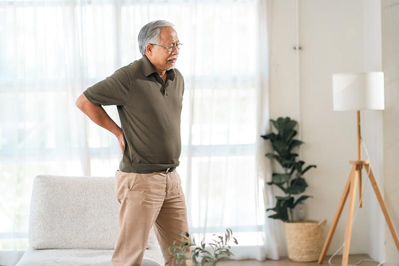 Man experiencing lower back pain at home from spinal stenosis.