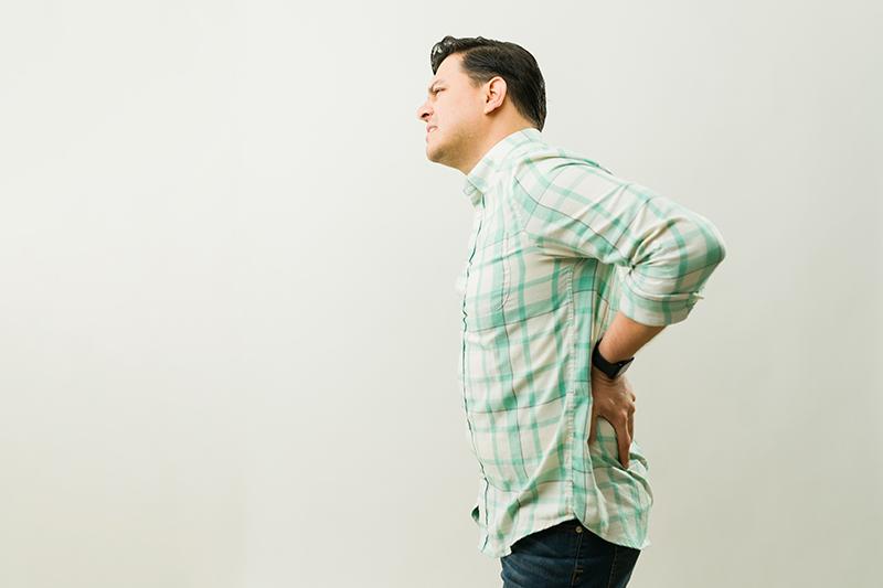 Man with spinal stenosis grimacing as he holds his lower back.