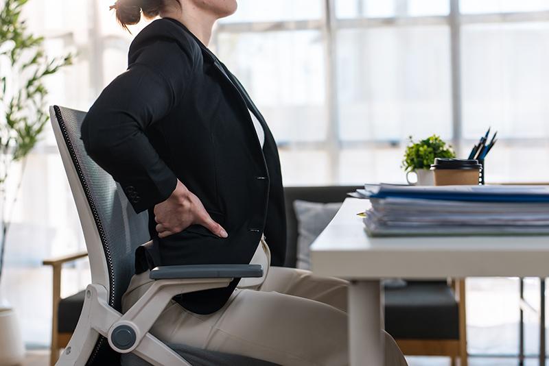 woman experiencing discomfort and pain in her lower back area while working in office