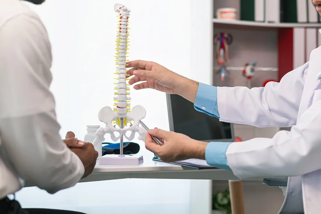A doctor referring to a model of the human spine in a consultation